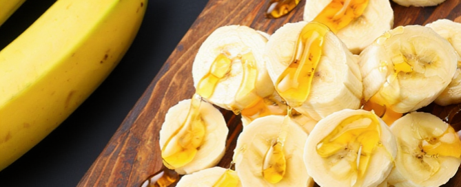 Bananes Del Monte Honeyglow entières et tranchées nappées de miel sur une planche en bois, présentation gourmande et naturelle.