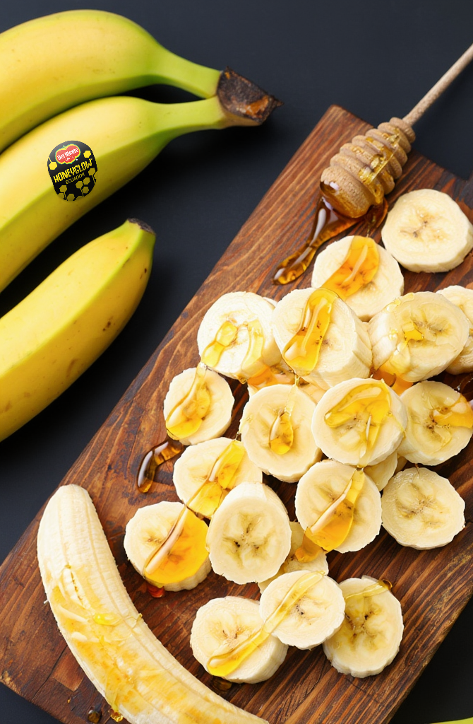 Bananes Del Monte Honeyglow entières et tranchées nappées de miel sur une planche en bois, présentation gourmande et naturelle.