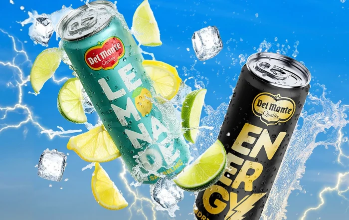 Two Del Monte 250ml cans—a lemon-lime lemonade drink and a black energy drink—floating with splashing water, ice cubes, citrus slices, and lightning in a bright blue background.